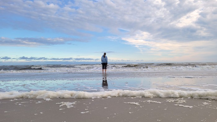 Ein Mann steht am Strand im Wasser und schaut auf den Ozean.