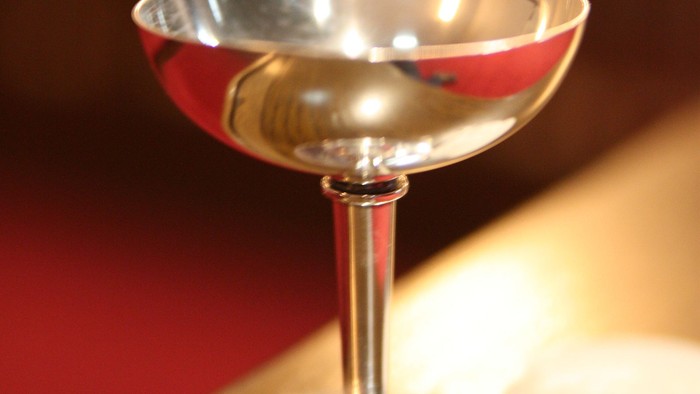 Et blank martini glas med en reflekterende overflade står elegant på en træoverflade ved siden af et stearinlys.
