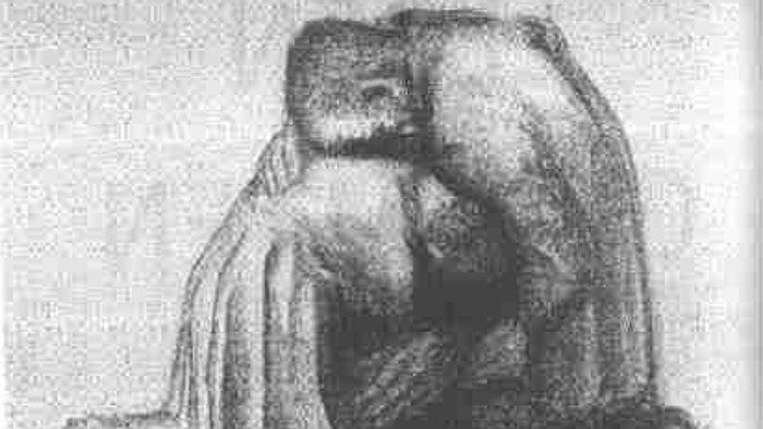 Ein Mann sitzt mit angezogenen Knien und umschlungenen Armen da.