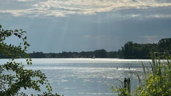 Ein ruhiger See unter einem bewölkten Himmel mit Sonnenstrahlen.