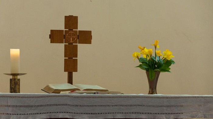 Auf einem Altar stehen ein Holzkreuz, eine brennende Kerze und eine Vase mit gelben Blumen