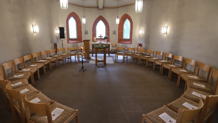 Ein runder Raum mit hölzernen Stühlen und einem zentralen Tisch, umgeben von bogigen Fenstern.