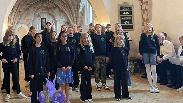 En gruppe af skolebørn og lærere samlet i en historisk hal.