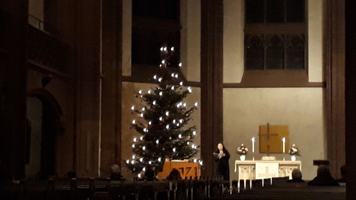 In der Kirche steht ein beleuchteter Weihnachtsbaum neben einem Altar mit Kerzen.