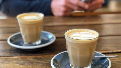 Zwei Tassen Kaffee auf Holztisch, Person nutzt Handy