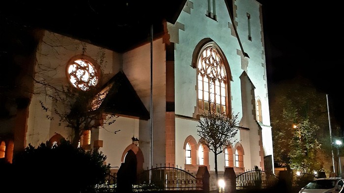 Kirchengrundstück bei Nacht mit beleuchteten Fenstern und Uhr