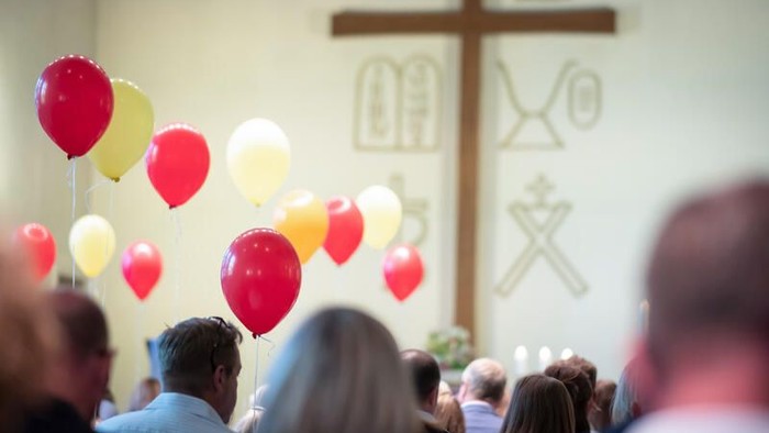 Eine Gruppe von Menschen in einer Kirche mit bunten Ballons und einem großen Kreuz im Hintergrund.