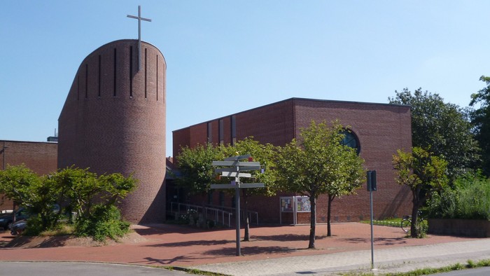 Modern Kirche mit hohem Turm und Kreuz, umgeben von Bäumen und Büschen