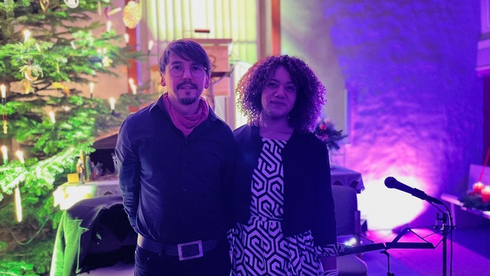 Zwei Personen stehen in der Nähe eines Weihnachtsbaums und eines Mikrofons.