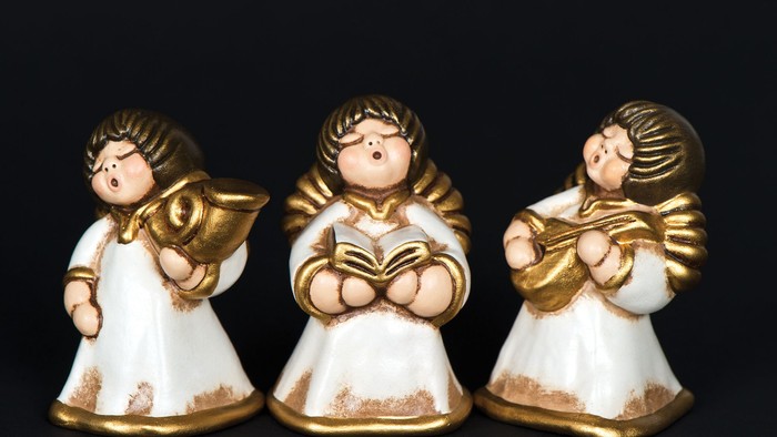 Tre lille engle af keramik med guldakcentuer, hver med vinger og musikinstrumenter, stå i en linje på sort baggrund.