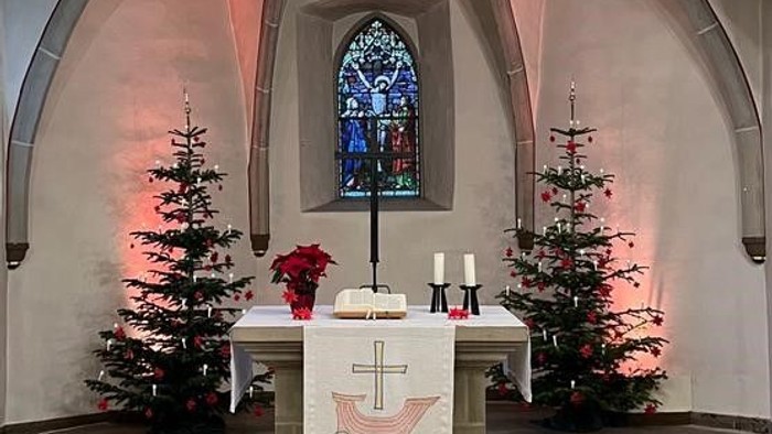 Kircheninneres mit Weihnachtsdekoration, darunter ein großer Stern, zwei Bäume und ein Altar mit Kerzen.