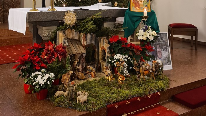 In der Kirche steht ein geschmückter Weihnachtsbaum neben einem Krippenszene-Diorama.