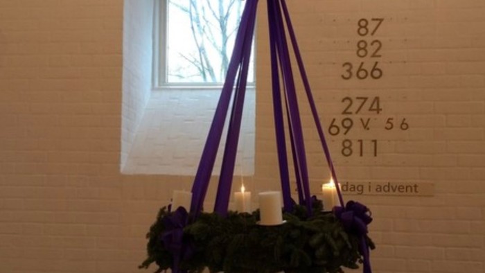 Adventskrans med lilla bånd og to ud af 4 hvide stearinlys tændt