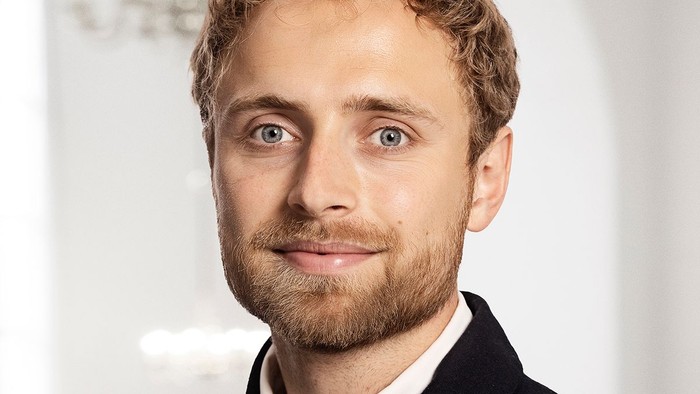 Professionel mand med kort krøllet hår iført en blazer og med et let smil.