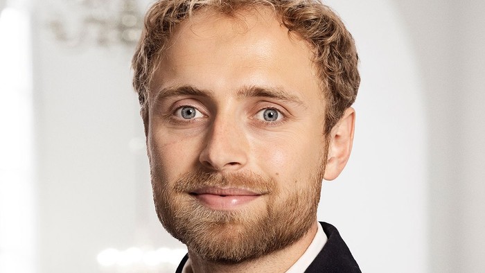 Professionel mand med kort krøllet hår iført en blazer og med et let smil.