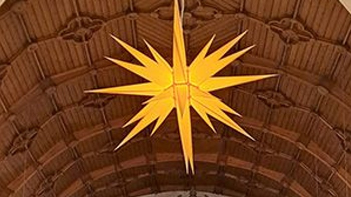 Ein großer Kircheninnenraum zeigt einen großen goldenen Stern, der über einer prächtigen Orgel hängt.