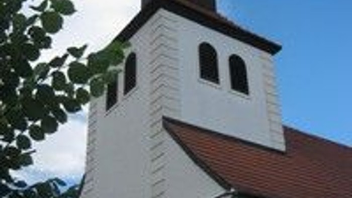 Weiße Kirche mit hohem Turm und roter Ziegeldach unter blauem Himmel