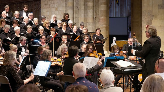 A choir and orchestra perform together in a grand, historic venue with an attentive audience.