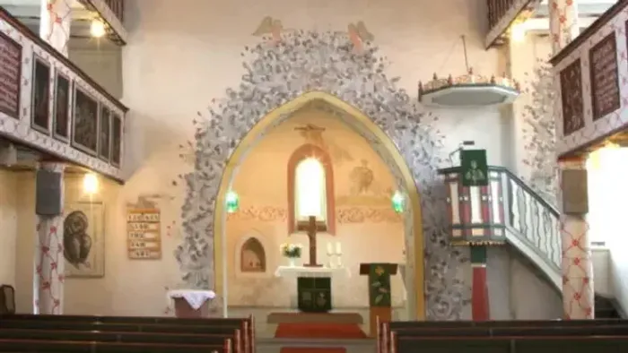 Kircheninneres mit aufwendigen Verzierungen, Empore und Buntglasfenstern.