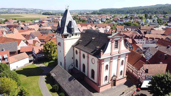 Ein weißer Kirchturm mit schwarzem Dach über einem Dorf mit roten Dächern.