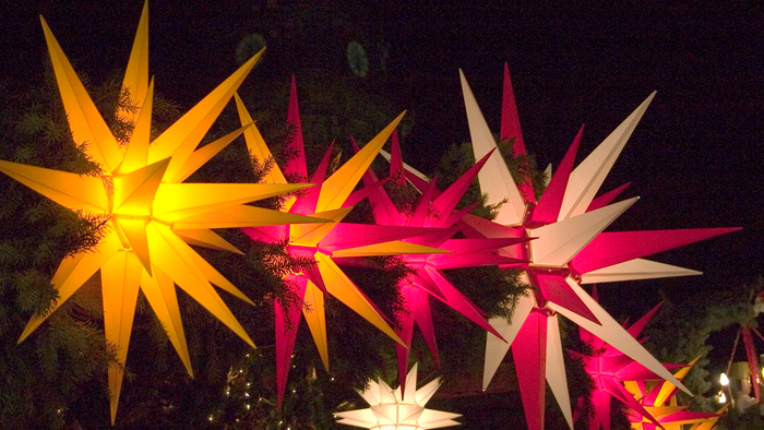 Bunte sternförmige Dekorationen, die nachts in einem Baum hängen.