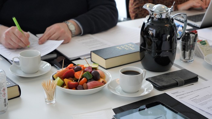 To dagslys lyser over bordet med dokumenter, frugt og kaffe.