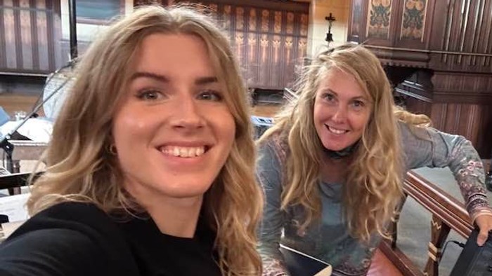 To kvinder smiler, mens de poser med et keyboardorgel i en prægtig indendørs omgivelse.