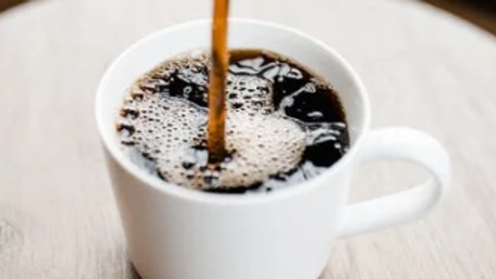 En lille hvid tekanne med kaffe, hvor der porres kaffe ind i.