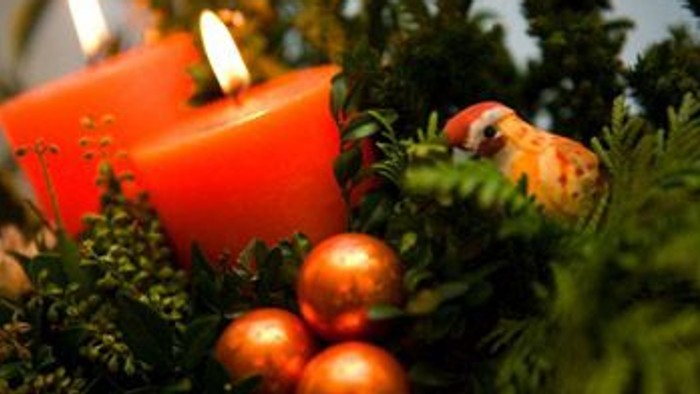 En rød lysestage med lyset slukket, omgivet af grønne planter og tre guldfarvede glaskugler.