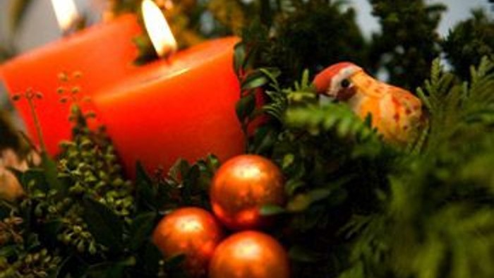 En rød lysestage med lyset slukket, omgivet af grønne planter og tre guldfarvede glaskugler.