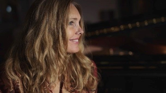 En kvinde med lang, blond hår sitter ved et piano i en koncertsal.