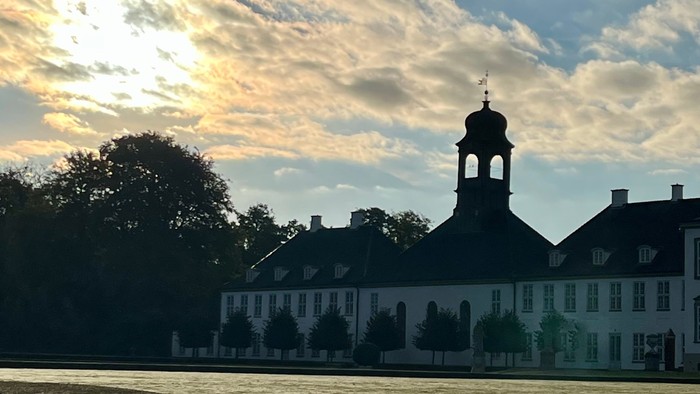 En stor bygning ved en sø med tårn og skyer i baggrunden