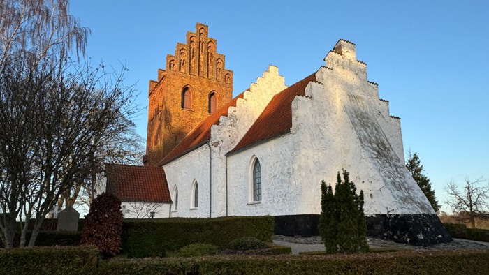 En hvid kirke med røde tag og en klokketårn i sollys.