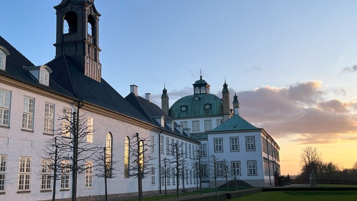 Stor historisk bygning med tårn og kuppelsaler ved solnedgang