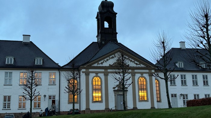 Stor hvid bygning med klokketårn og lysende vinduer.