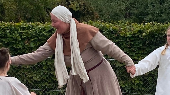 Børn, der holder hinanden i hånden i historiske kostumer udendørs.