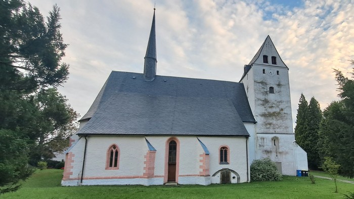 Kleine weiße Kirche mit hohem Turm auf grünem Hügel