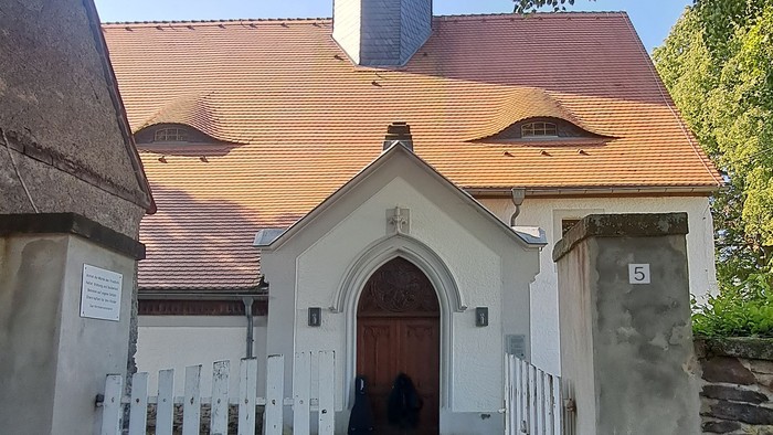 Kleine Kirche mit weißem Zaun und rotem Dach.