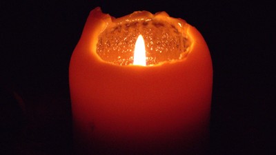 Eine einzige brennende Kerze in der Dunkelheit.