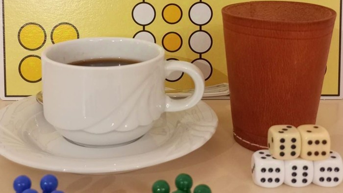 Ein weißer Kaffeebecher auf einem Teller, ein brauner Becher, Würfel und Spielsteine auf einem gelben Hintergrund mit geometrischen Mustern