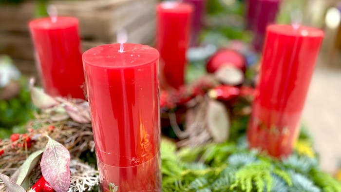 Lebendig rote Kerzen, arrangiert in einem festlichen Kranz, umgeben von Grünzeug und getrockneten Blumen.