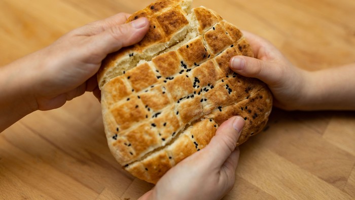Zwei Hände halten ein Sesambrötchen auf einem Holztisch