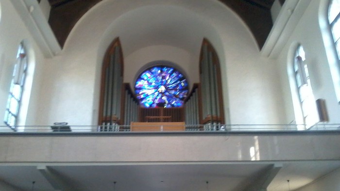 Die Kirche hat ein großes Rundbogenfenster und eine Empore mit Orgel.