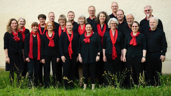Ein Chor steht im Freien vor einer Wand und posiert für ein Gruppenfoto.