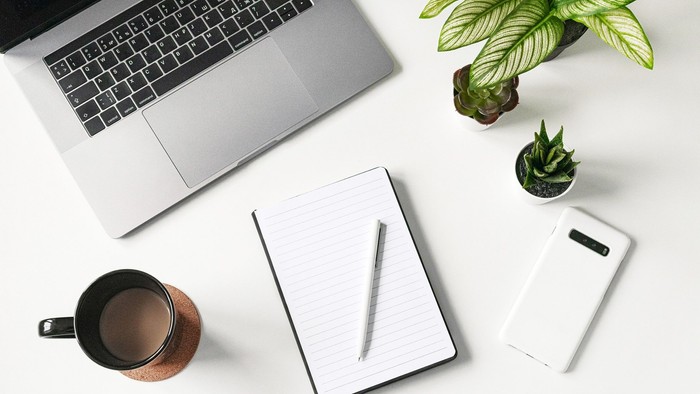 Bureau med laptop, notatbog, pen, mobiltelefon, kaffe og planter