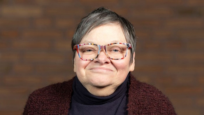 Eine Frau mit kurzem Haar und bunten Brillen lächelt.