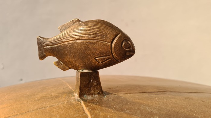 Ein Bronzefisch steht auf einem Sockel auf einem Holztisch.