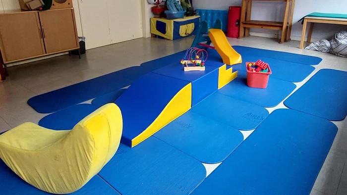 Ein Kinderzimmer mit blauen Matten, gelben Kissen und Spielzeug.