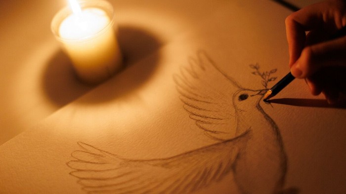 Eine Person zeichnet einen Vogel im Sand bei Kerzenlicht