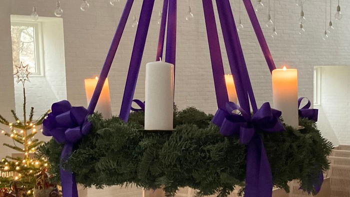 En hængende juledekoration med grønne blomster og lilla bånd, med lysede lygter og en kranse.